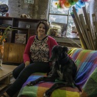 Woman in a pink cardigan on a brightly covered sofa with a black dog