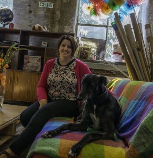 Woman in a pink cardigan on a brightly covered sofa with a black dog